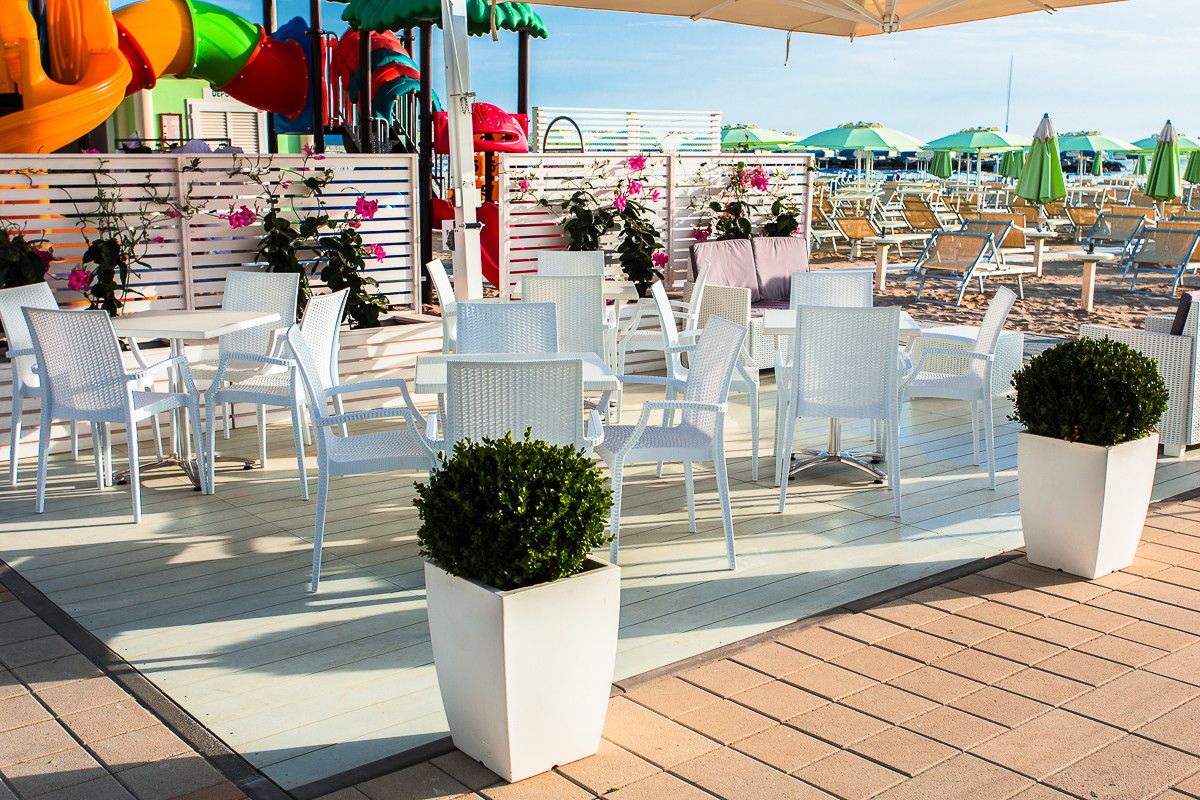 Terrazza del Coconut con tavoli e sedie bianche, piante e fiori, davanti alla spiaggia