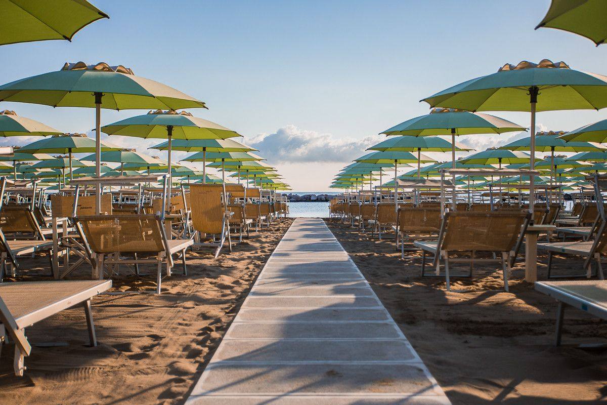 Camminamento in legno tra file di ombrelloni verdi e lettini, verso il mare di Bellaria-Igea Marina