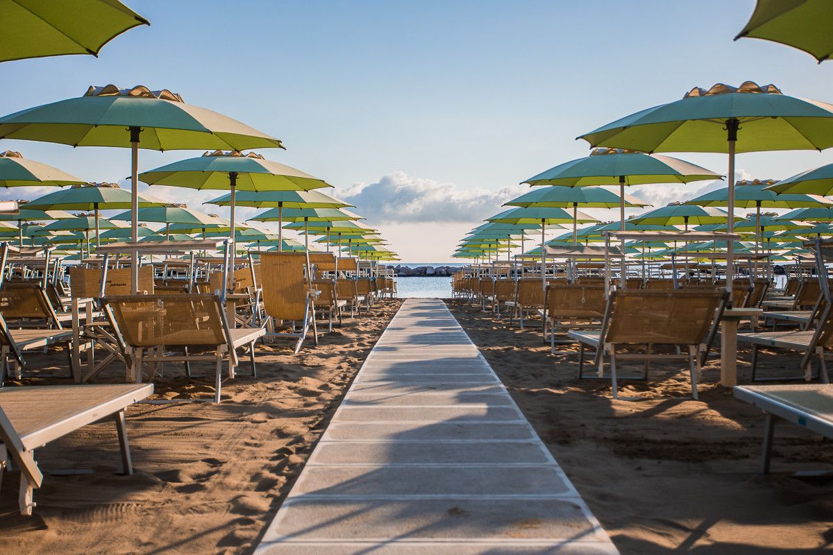 Camminamento in legno tra file di ombrelloni verdi e lettini, verso il mare di Bellaria-Igea Marina